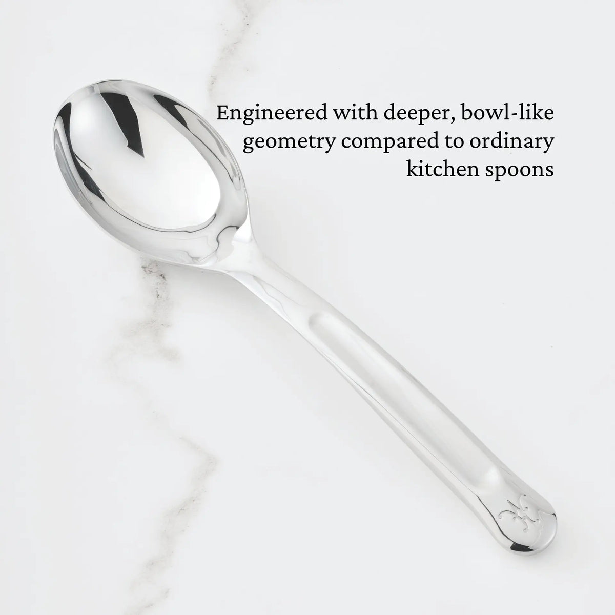 A 10.5-inch Stainless Steel Solid Serving Spoon from Hestan Provisions® with a deep, bowl-like shape rests on a white marble surface. Text above the spoon reads: Engineered with deeper, bowl-like geometry compared to ordinary kitchen spoons—an essential addition to any chef’s tools from the Hestan Provisions® Serving Tools collection.