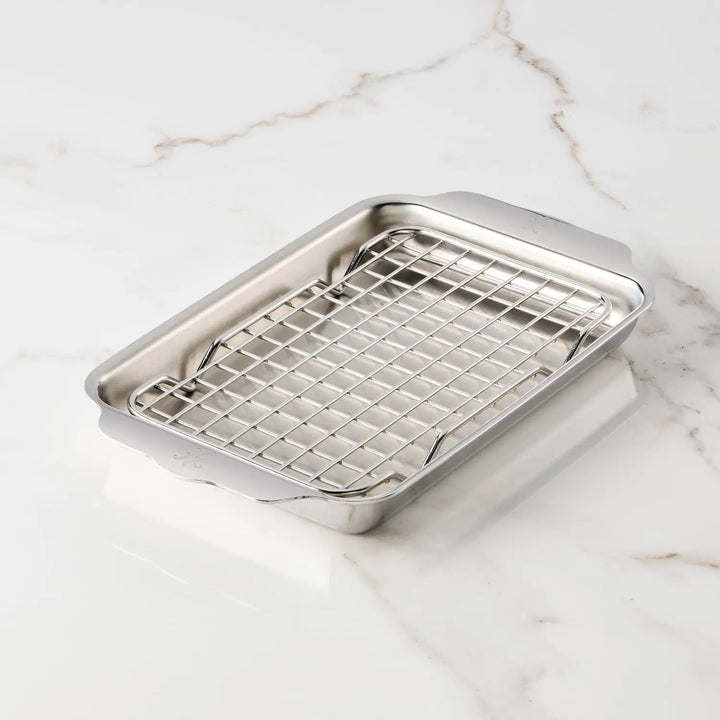 The Hestan OvenBond Tri-ply Mini Eighth Sheet Pan with Rack is a rectangular stainless steel pan with an oven-safe rack, shown on a white marble surface.