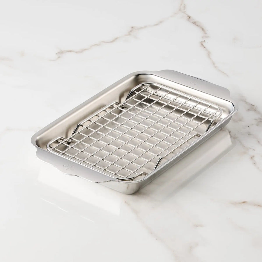 The Hestan OvenBond Tri-ply Mini Eighth Sheet Pan with Rack is a rectangular stainless steel pan with an oven-safe rack, shown on a white marble surface.