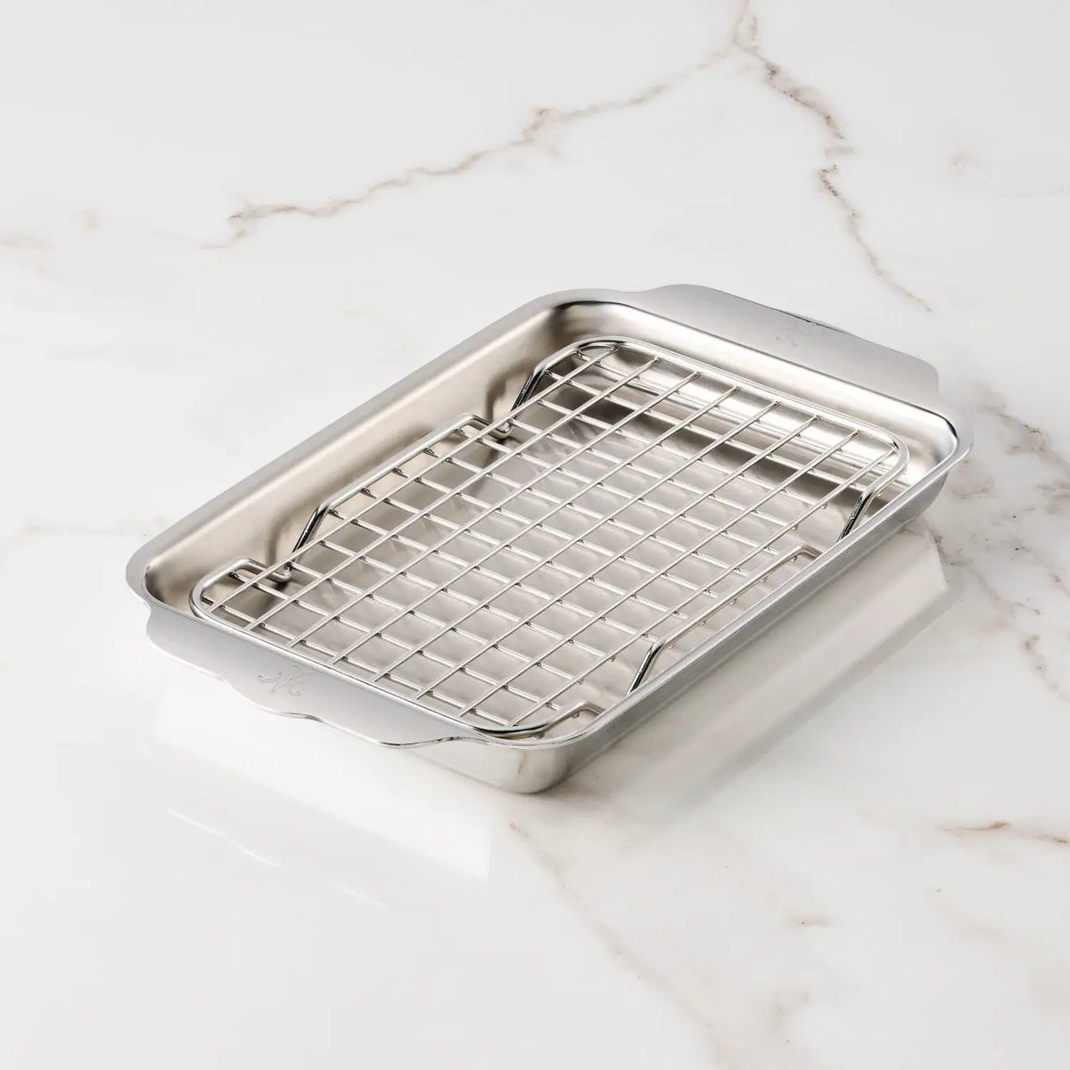 The Hestan OvenBond Tri-ply Mini Eighth Sheet Pan with Rack is a rectangular stainless steel pan with an oven-safe rack, shown on a white marble surface.