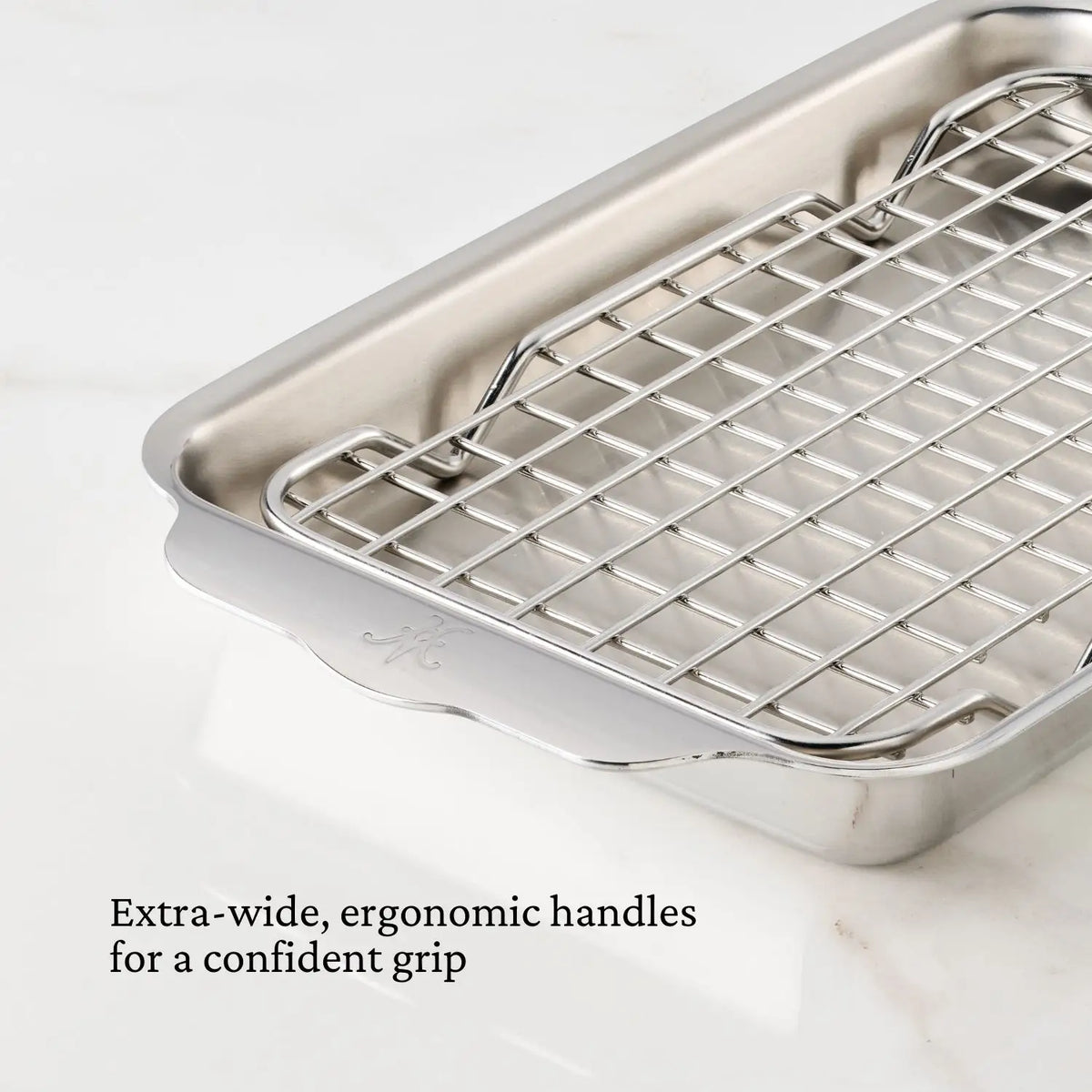 The Hestan OvenBond Tri-ply Mini Eighth Sheet Pan with Rack is shown on a white surface, featuring extra-wide, ergonomic handles for a confident grip. The stainless steel pan includes a removable, oven safe rack and wide, curved handles.
