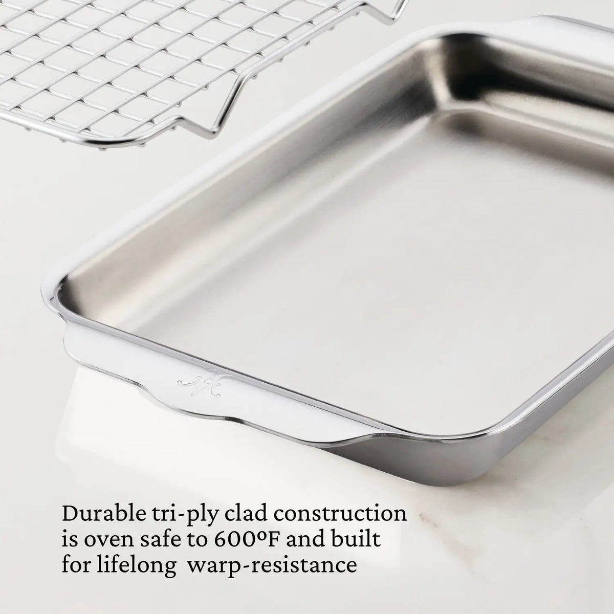 The Hestan OvenBond Tri-ply Mini Eighth Sheet Pan with Rack, crafted with tri-ply clad construction, is warp-resistant and oven safe to 600°F. It sits on a white surface with its oven-safe rack above it.