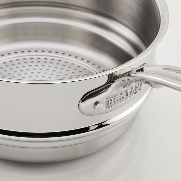 A close-up of the Stainless Steel Steamer Insert, 3-Quart by Hestan Provisions shows its durable design. The handle is engraved with HESTAN Provisions, and the polished surface reflects light beautifully as it sits on a white background.