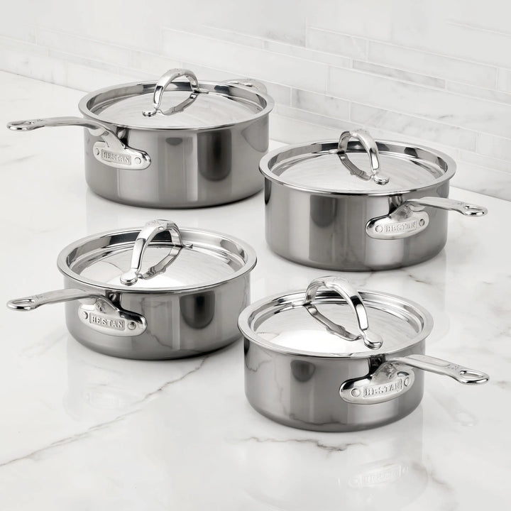 Four NanoBond Titanium Saucepans with lids are neatly arranged on a marble countertop. Each saucepan features a shiny finish, sturdy handles, and is metal utensil safe. A sleek white tiled wall provides the perfect backdrop.