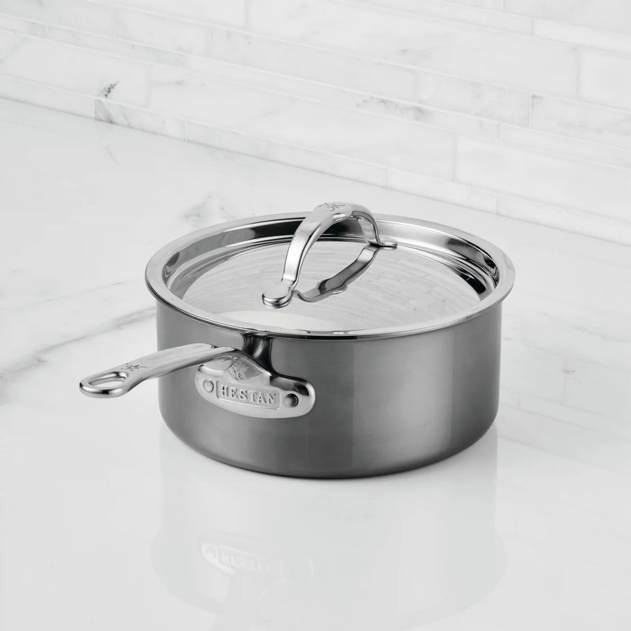 A NanoBond Titanium Saucepan with a lid and long handle sits on a white marble countertop, set against a light-colored tiled backsplash.