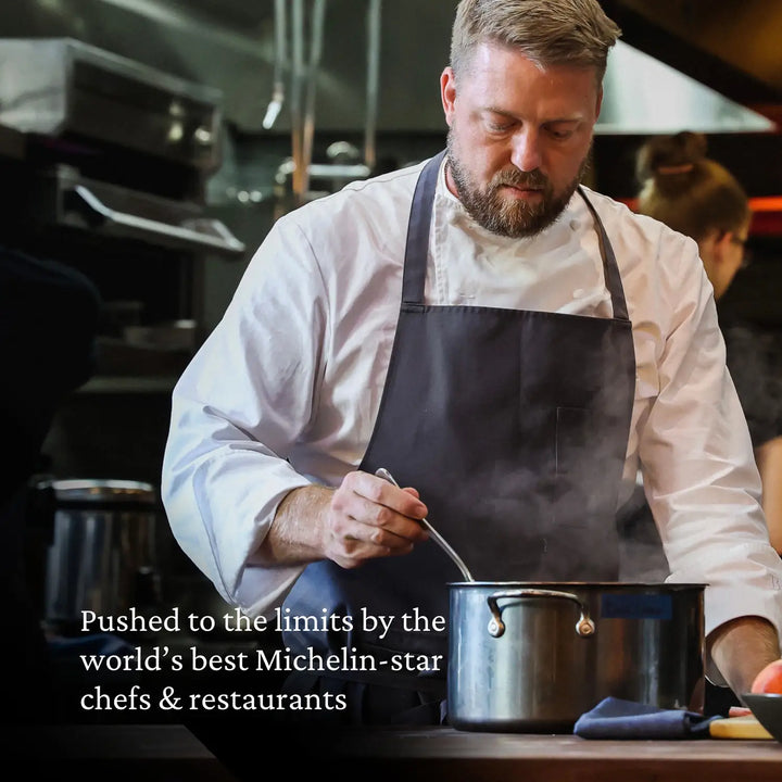 A male chef in a white jacket and dark apron stirs a large NanoBond Titanium Stockpot on a stovetop in a professional kitchen. Text overlay: Pushed to the limits by the world’s best Michelin-star chefs & restaurants.