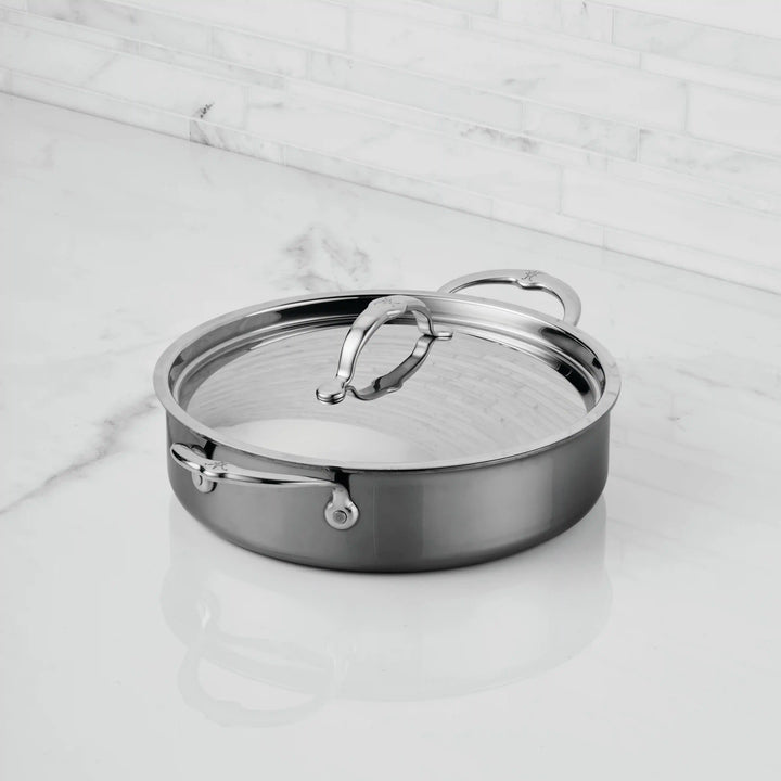 The NanoBond Titanium Rondeaus with Lids, featuring two handles, sits on a white marble countertop with a white tile backsplash, highlighting the elegance of this advanced cookware.