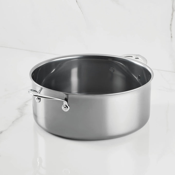 A NanoBond Titanium Rondeau with lid and two handles sits on a white marble countertop, complemented by a matching white marble backsplash in the background.