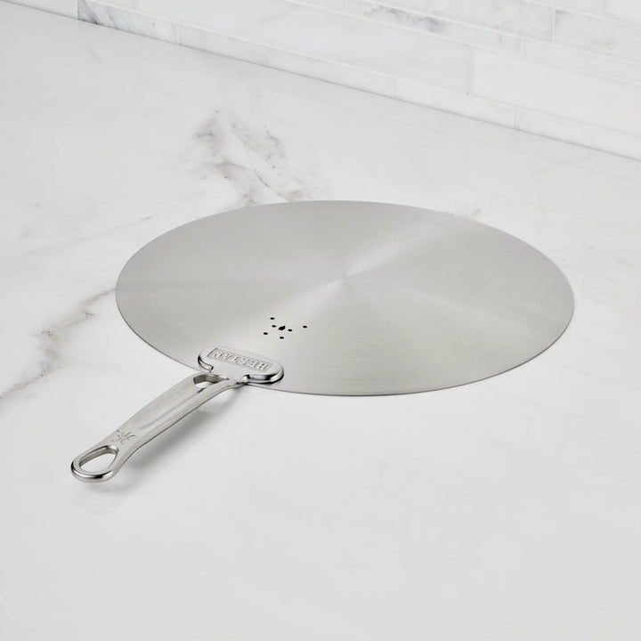 The Hestan Provisions Stainless Steel Universal Lid rests flat on a white marble countertop, blending into your eco-friendly kitchen with its dishwasher-safe design and built-in splatter screen.