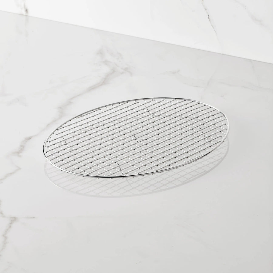 A 17.5-inch by 14-inch oval rack from the Hestan Provisions® Clad Oval Roaster & Rack set rests on a white marble surface. Expertly crafted from durable 18/10 stainless steel, this lightweight rack features thin, intersecting metal wires in a sturdy crisscross pattern.