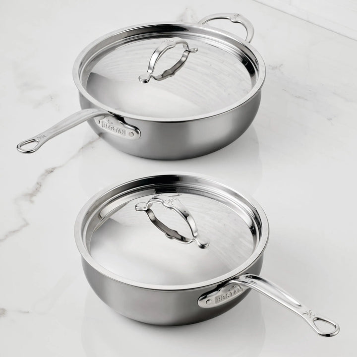 Two Titanium Essential Pans with lids by NanoBond sit on a white marble countertop. The stainless steel sauté pans feature long handles, matching metal lids with handles, and are marked with the NanoBond brand name.