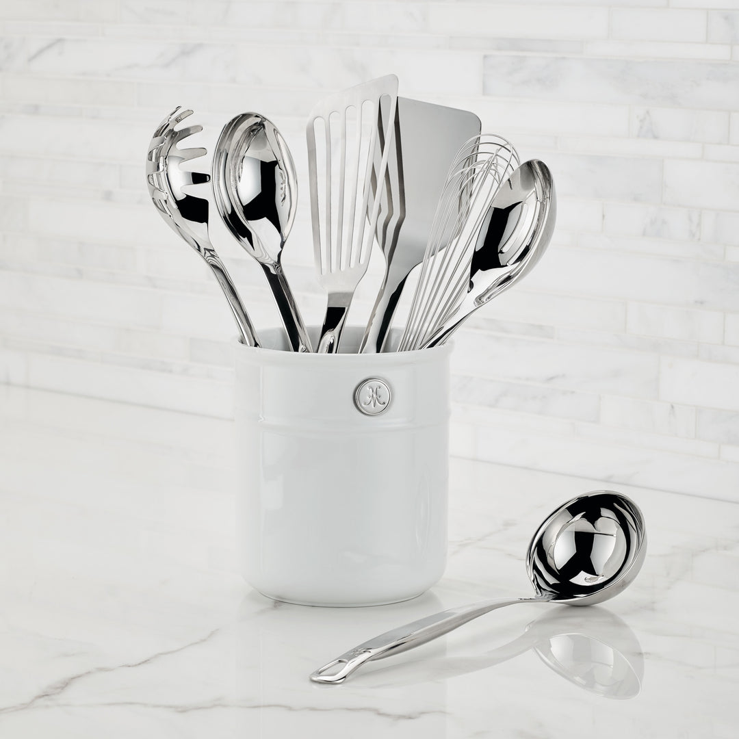 The Ultimate Chefs Tool Set, an 8-piece 18/10 stainless steel collection by Hestan Provisions, is inspired by Michelin-starred chefs and stands in a white ceramic holder against a white tiled wall. A ladle rests on the counter beside the holder.