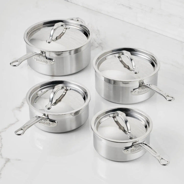 Four ProBond® Forged™ Brushed Clad Stainless Steel Saucepans, each a different size with matching lids and long handles, are arranged on a white marble countertop.