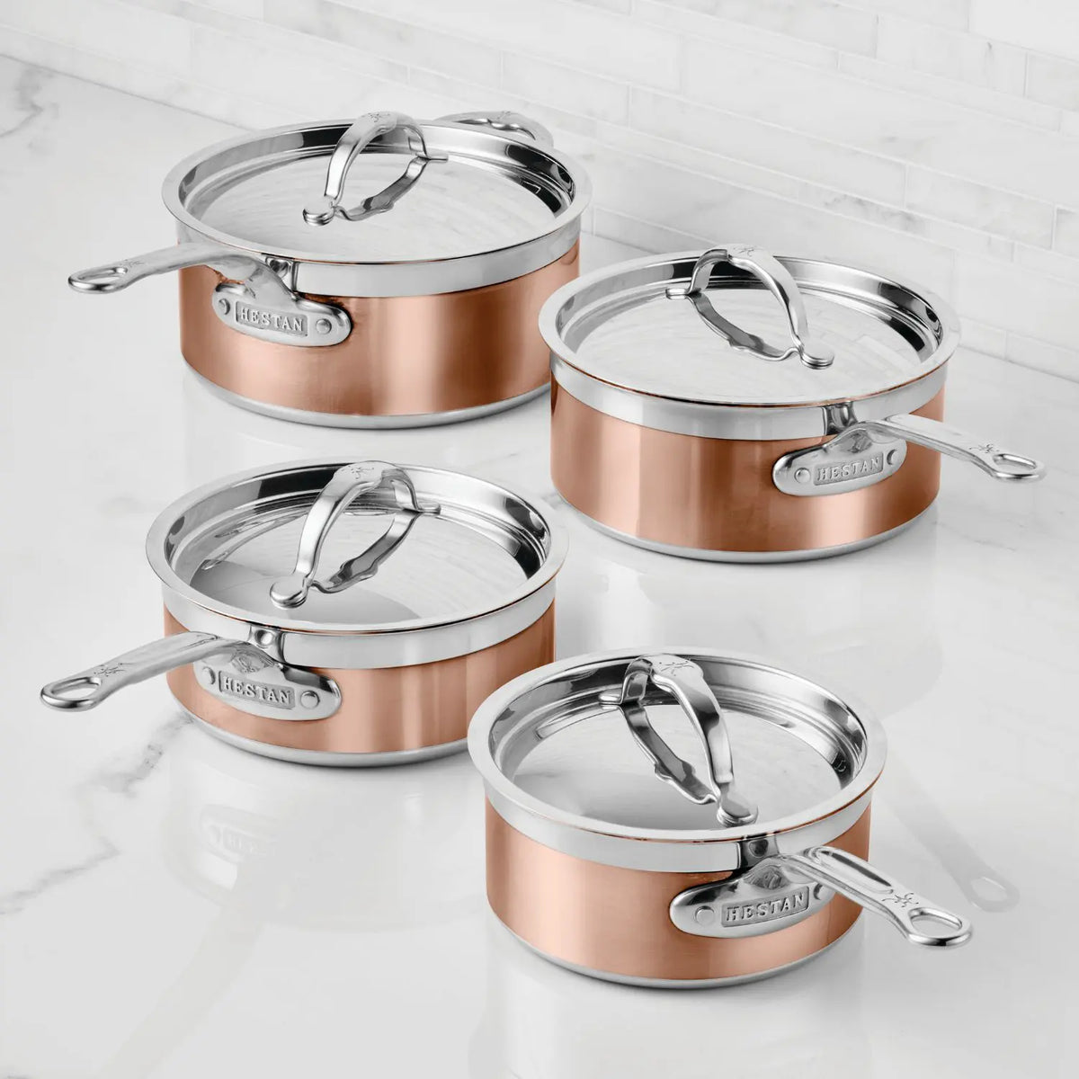 Four CopperBond Copper Induction Saucepans, featuring a 100% copper core, stainless steel, and metal handles, are displayed on a white marble countertop. Each saucepan shows the CopperBond brand label on the side.