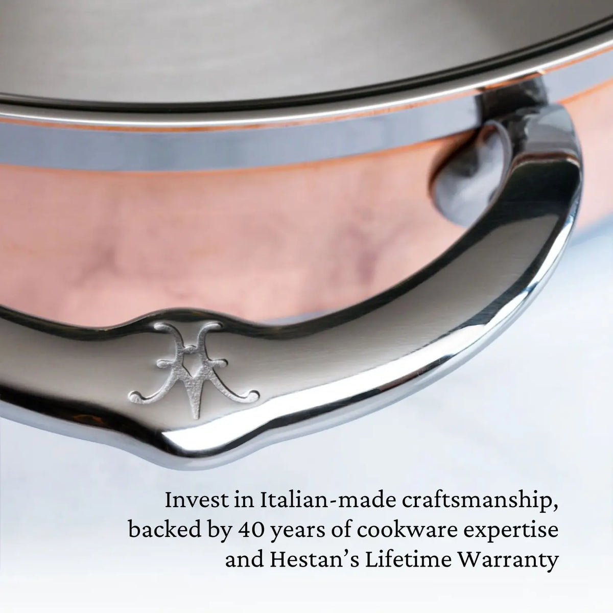 Close-up of a shiny CopperBond Copper Induction Braiser with Lid, 3.5-Quart handle engraved with the logo, attached to a copper pot. Features Italian-made craftsmanship, 40 years expertise, and Hestan’s lifetime warranty.