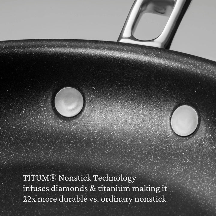 Close-up of a black nonstick frying pan with metal handle and rivets, showing textured surface. Features TITUM nonstick tech with diamonds and titanium—perfect for any Thomas Keller Commercial Clad Stainless Steel 29-Piece Cookware Set.