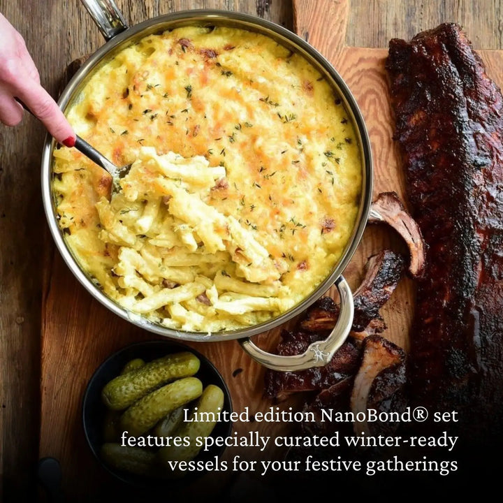 A large pan of baked macaroni and cheese sits next to a rack of ribs, sliced smoked sausage, and pickles on a wooden board. A hand serves macaroni from the pan. Text at the bottom highlights the innovative NanoBond® Titanium x Tyler Florence Cookware Set, 41-Piece, acclaimed for its advanced use of Molecular Titanium for exceptional durability and performance.
