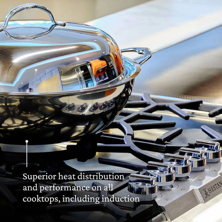 A stainless steel pot with a lid sits on a gas stove burner. Text on the image reads: Enjoy superior heat distribution and performance on all cooktops—including induction—thanks to NanoBond®’s innovative Molecular Titanium technology featured in the Titanium x Tyler Florence Cookware Set, 41-Piece.