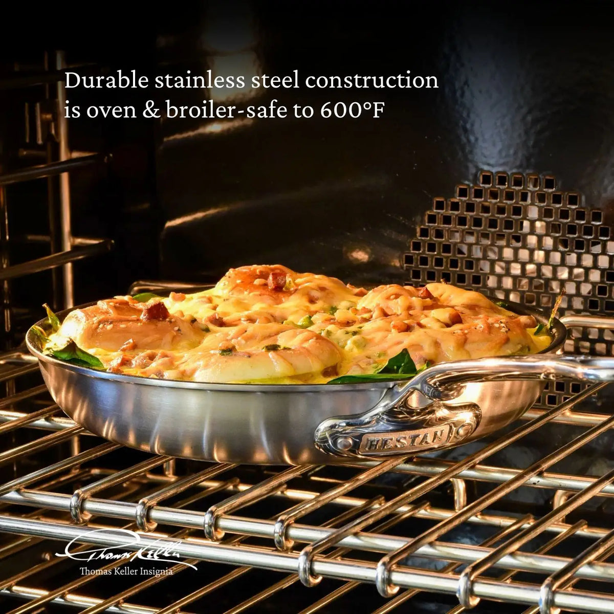 A Commercial Clad Stainless Steel 10-Piece Cookware Set pan from Thomas Keller Commercial Clad holds baked food topped with melted cheese on an oven rack. Text highlights its durable tri-ply build and oven/broiler safety up to 600°F.