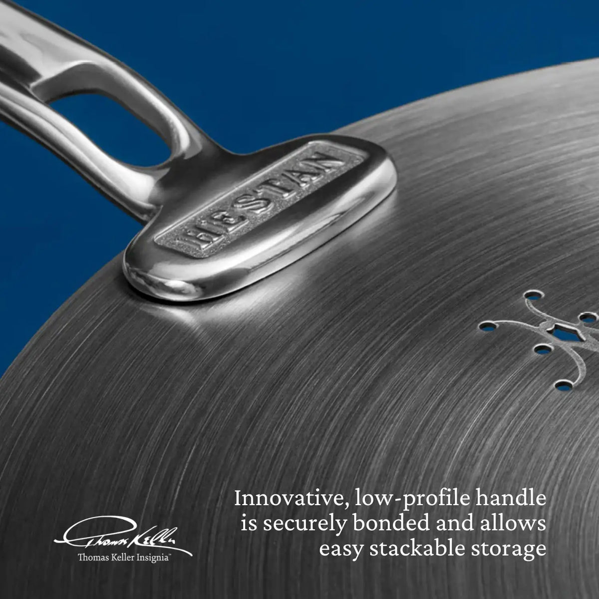 Close-up of a stainless steel pan from the Thomas Keller Commercial Clad Stainless Steel 10-Piece Cookware Set, featuring a HESTAN-engraved handle and a brushed finish that highlights its innovative, stackable design for easy storage.