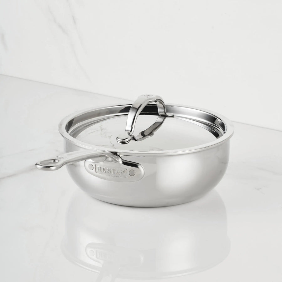 The ProBond® Luxe™ Polished Clad Stainless Steel Saucier Pan, 2-Quart, with lid and sturdy handle, sits on a white marble countertop against a matching marble wall.