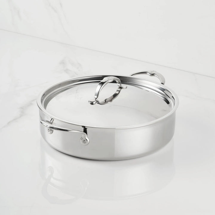 A ProBond® Luxe™ Polished Clad Stainless Steel Rondeaus with Lid, featuring two side handles and a lid handle for easy lifting, sits on a white marble surface.