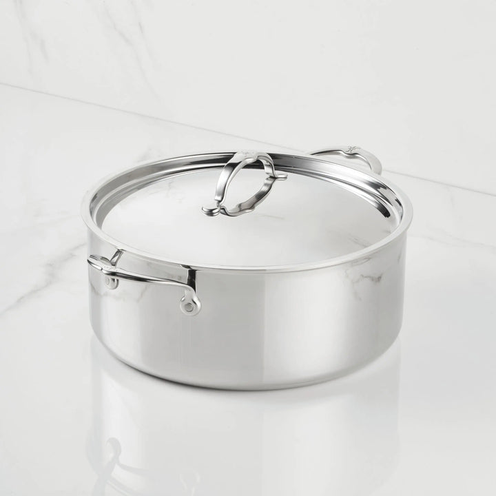 A ProBond® Luxe™ Polished Clad Stainless Steel Rondeau with a fitted lid and sturdy handles, elegantly placed on a white marble surface.