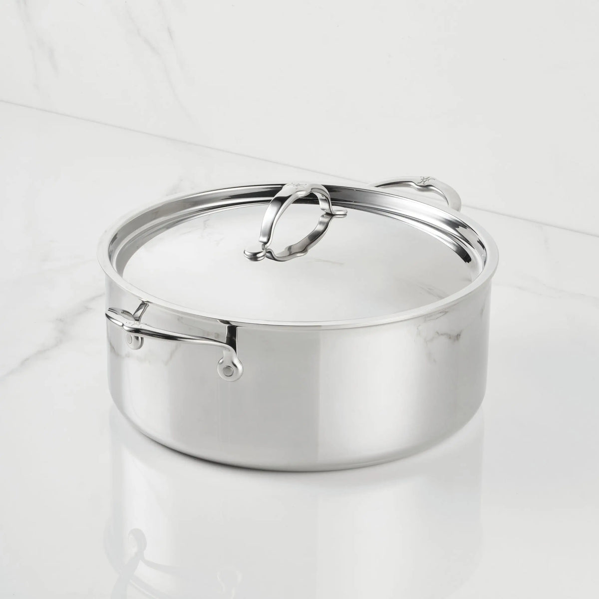 A ProBond® Luxe™ Polished Clad Stainless Steel Rondeau with a fitted lid and sturdy handles, elegantly placed on a white marble surface.