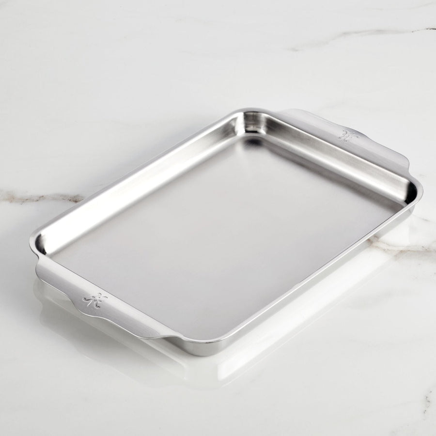 The Hestan OvenBond Tri-Ply Quarter Sheet Pans & Rack, 9-in x 12-in, features raised edges and two handles, elegantly showcased on a white marble surface.