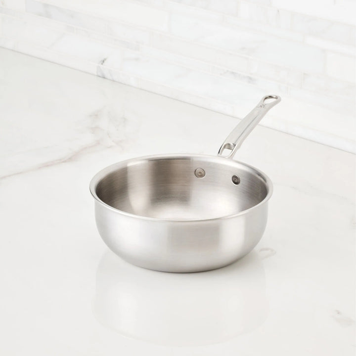 A Thomas Keller Commercial Clad Stainless Steel 2-Quart Saucier sits clean and empty on a white marble countertop, ready to deliver professional performance in any kitchen.