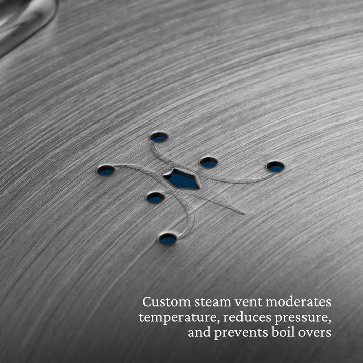 Close-up of brushed metal shows a custom steam vent with small symmetric holes. Text: The Thomas Keller Commercial Clad Stainless Steel 11-Piece Cookware Set features vents that control temperature and prevent boil overs.
