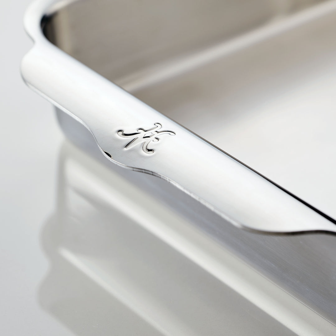 Close-up of a stainless steel tray with a decorative edge featuring an engraved monogram. The shiny surface reflects light, highlighting the smooth texture and polished finish. The background is a soft, pale gray.
