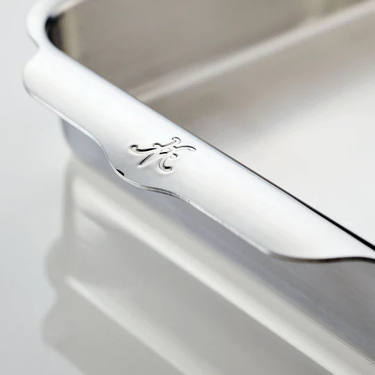 Close-up of a polished silver tray with a scalloped edge, featuring an engraved letter K on the corner. The background reflects the trays shiny surface.