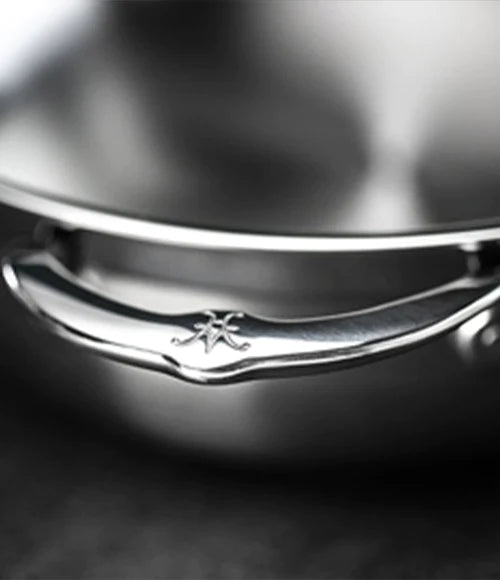 Close-up image of a shiny, metallic handle attached to a polished surface, likely a kitchen pot or pan. The handle has a subtle engraved design. The background is blurred, focusing attention on the handle.