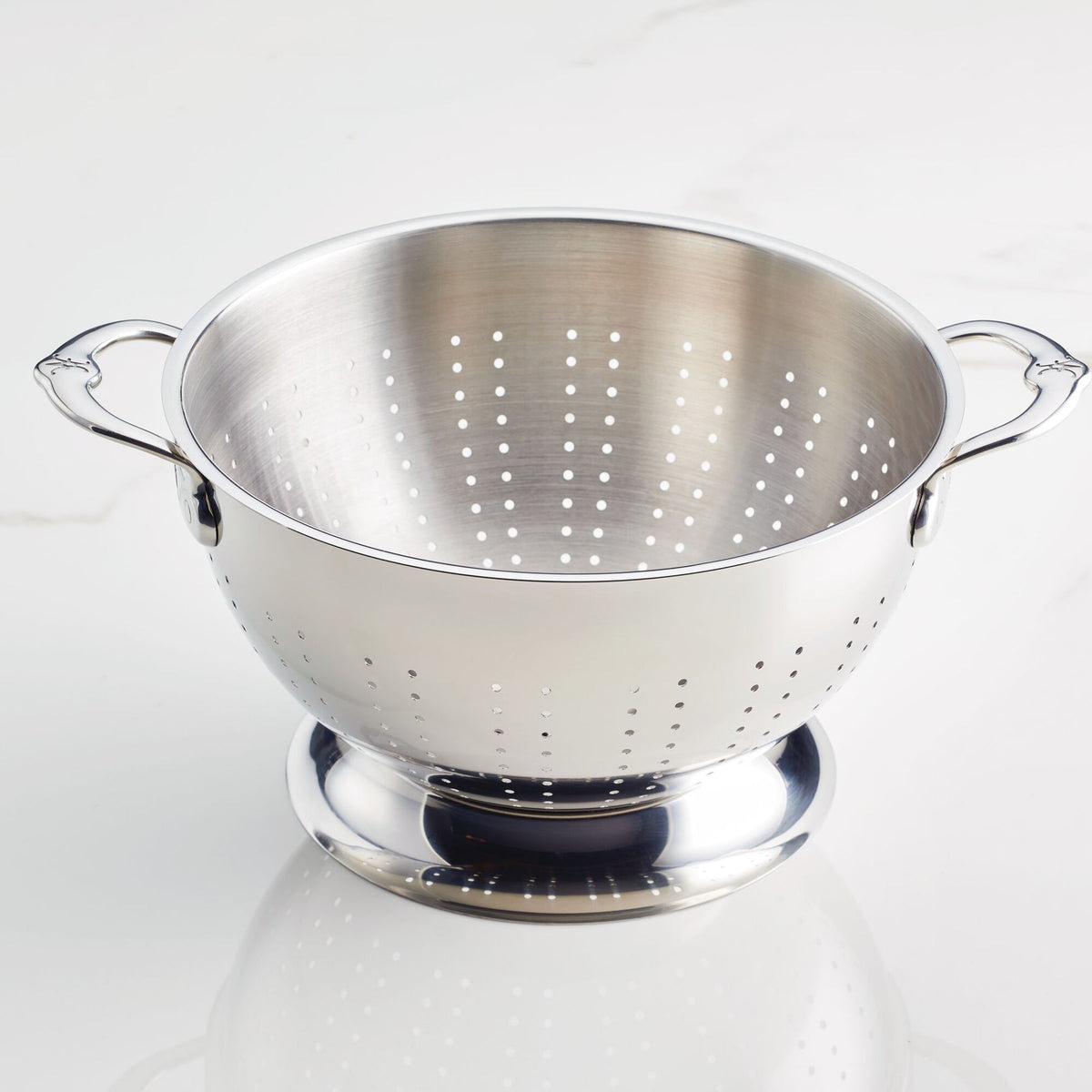The Hestan Provisions Stainless Steel Colander Set, 2-Piece, is shown on a light surface with ergonomic handles and a raised base, featuring dishwasher-safe construction and perforations for efficient draining.